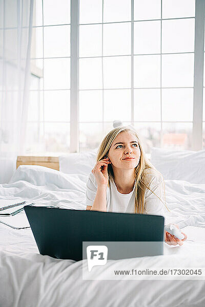 blonde girl working on laptop in bed