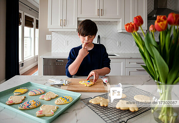 Junger Junge beim Verzieren von Osterkeksen auf dem Tresen einer modernen Küche.