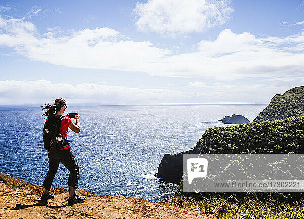 Frau macht Handy-Foto beim Wandern in der Nähe des Ozeans auf Hawaii