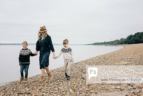 Mutter  die mit ihren Kindern am Strand spazieren geht und lächelnd die Hände hält