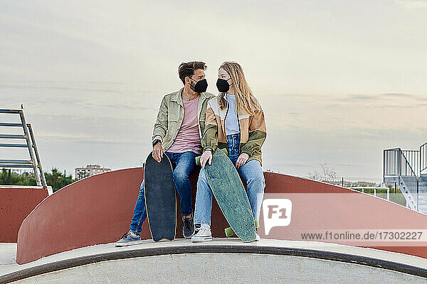 Junges Paar mit Masken schaut sich in einem Skatepark an