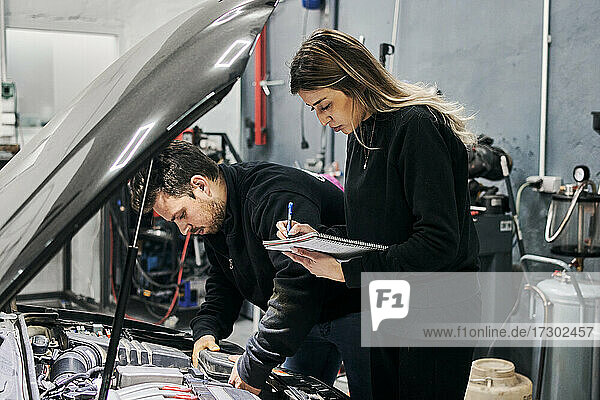 Männlicher Mechaniker bringt weiblichen Mechanikern bei  wie man ein Fahrzeug repariert