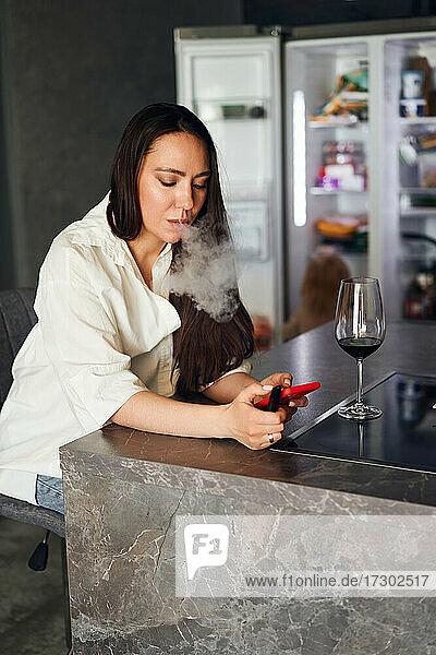 schöne brünette Frau raucht eine elektronische Zigarette trinkt Wein