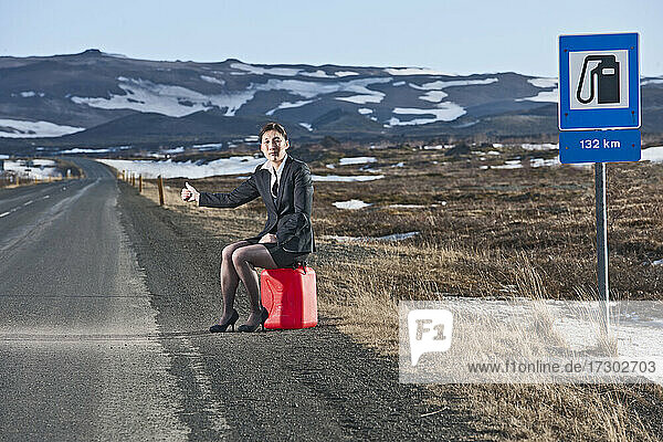 Geschäftsfrau  die auf einem Benzinkanister sitzt und versucht  in Island zu trampen