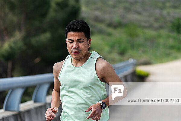 Nahaufnahme eines jungen lateinamerikanischen Läufers  der auf einer Brücke läuft.