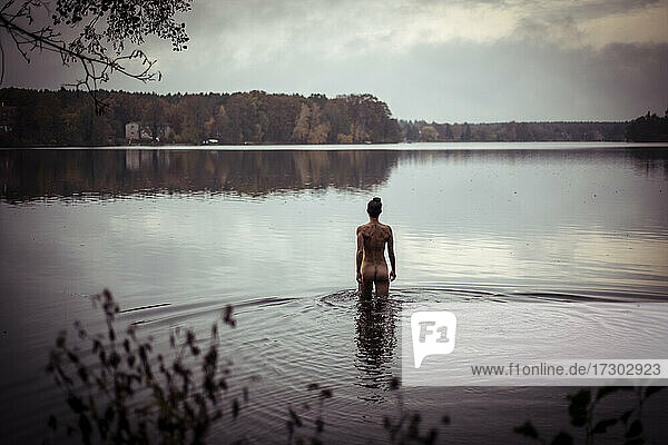 Starke androgyne Frau geht nackt in natürlichen See in Deutschland