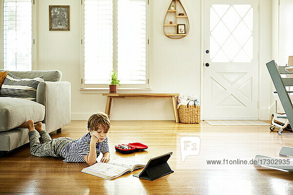 Junge auf Hartholzboden liegend beim Lernen im Wohnzimmer zu Hause
