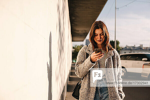 Glückliche Frau mit Smartphone auf der Straße in der Stadt