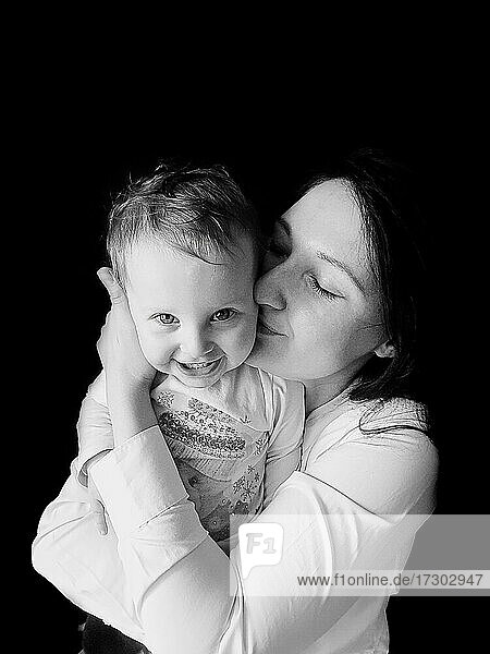 Schwarz-Weiß-Porträt einer Mutter  die ein lächelndes Mädchen umarmt und küsst