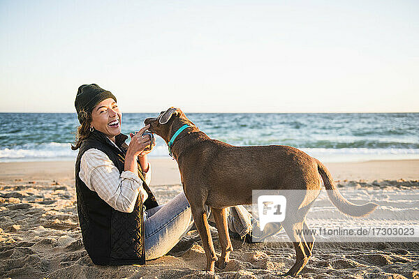 Junge Frau  die ein Getränk aus einem Becher genießt  während sie mit ihrem Hund am Strand zeltet