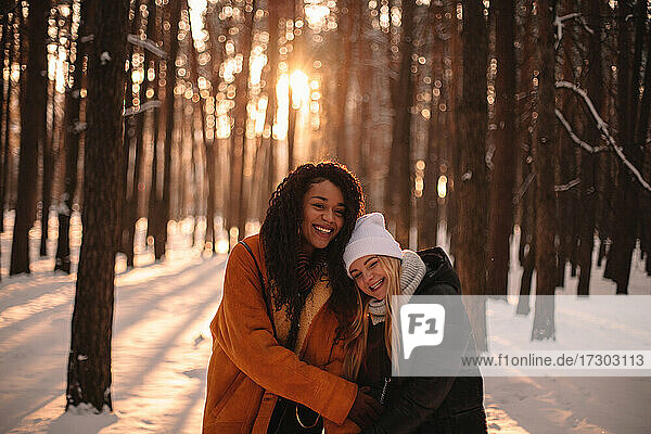 Portrait of happy girlfriends embracing while standing in snowy park