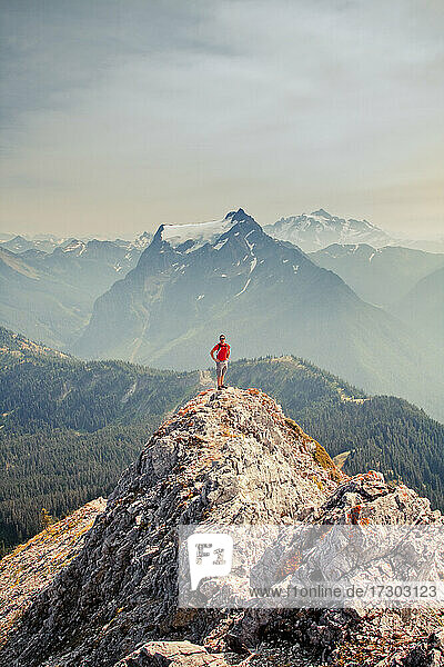 Wanderer mit rotem Hemd steht auf einem Berggipfel mit malerischer Aussicht dahinter