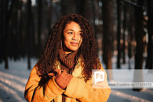 Glückliche junge Frau  die im Winter im Park steht und die Sonne betrachtet