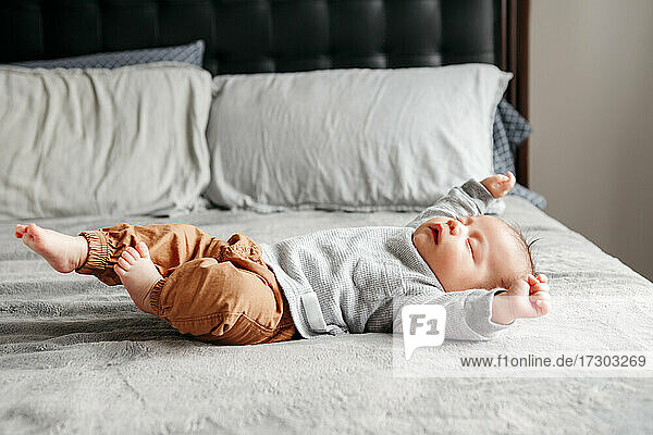 Cute funny newborn baby boy sleeping on bed at home and stretching.