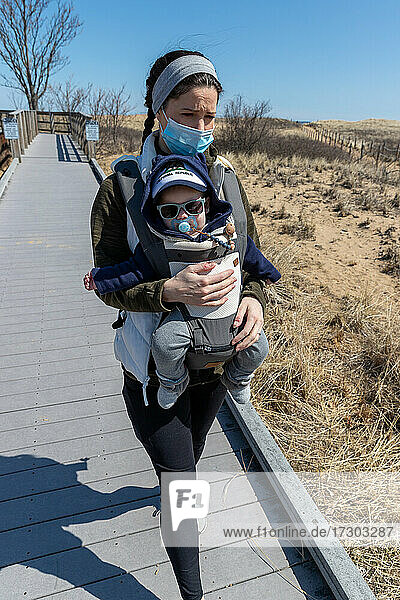 Mother wearing mask walking baby along beach boardwalk.