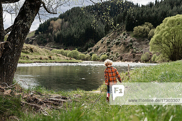 Small child holding stick walking near water in New Zealand