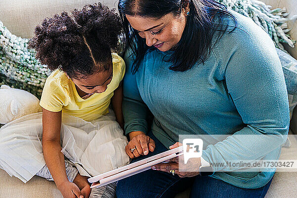Großmutter zeigt ihrer Enkelin ein digitales Tablet  während sie gemeinsam ihre Freizeit zu Hause verbringen