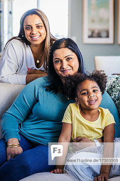 Porträt eines lächelnden Mädchens mit Mutter und Großmutter auf dem Sofa zu Hause