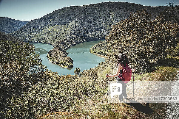 Frau mit Rucksack auf dem Gipfel eines Berges mit Blick auf den Fluss
