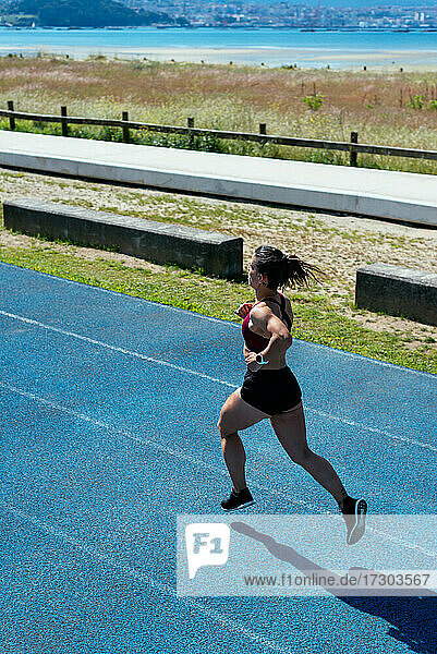 Rückenansicht einer jungen Sprinterin beim Laufen auf einer Leichtathletikbahn