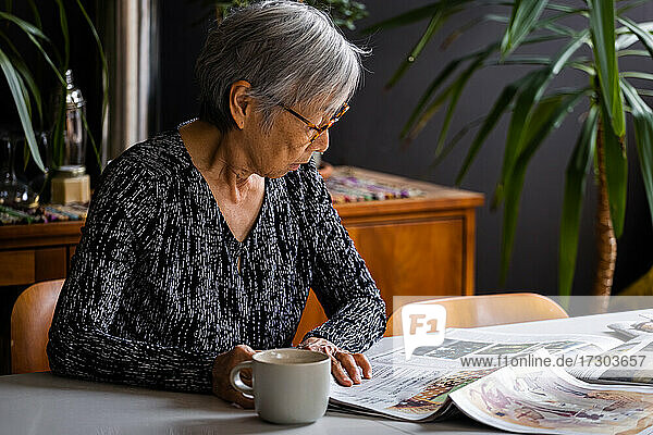 Senior woman reading newspaper while sitting at table with coffee