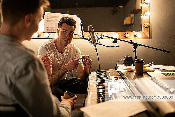 Mann im Gespräch mit einem Kollegen in der Nähe des Digitalpianos während einer Pause im Aufnahmestudio