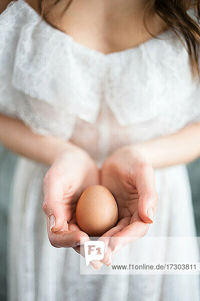 Osterei in den Handflächen einer Frau in einem weißen Kleid  Nahaufnahme.