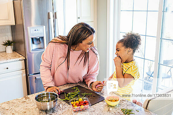 Cheerful mother and daughter preparing food at home