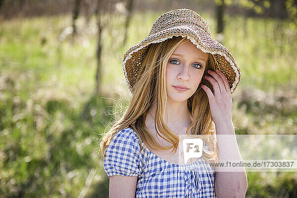 Beautiful teen blond girl outdoors in sundress and sun hat  backlit.