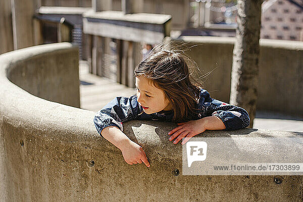 Ein kleines Mädchen lehnt sich an einem windigen  sonnigen Tag über eine gebogene Steinmauer