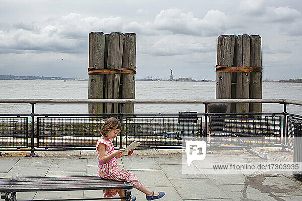 Ein kleines Kind sitzt auf einer Bank am Hudson mit Blick auf die Freiheitsstatue