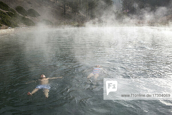 Zwei Kinder schwimmen in einem Pool von Trinity Hot Springs  aus dem Dampf aufsteigt