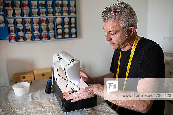 ein Schneider bei der Arbeit mit seiner Nähmaschine in seiner kleinen Werkstatt