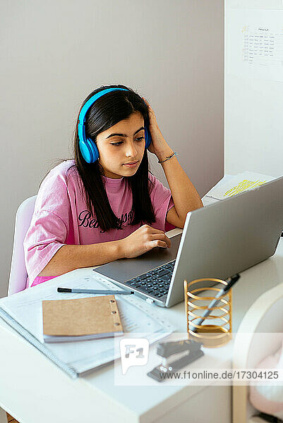 Konzentrierter Teenager  der am Schreibtisch lernt und im eigenen Zimmer Musik hört