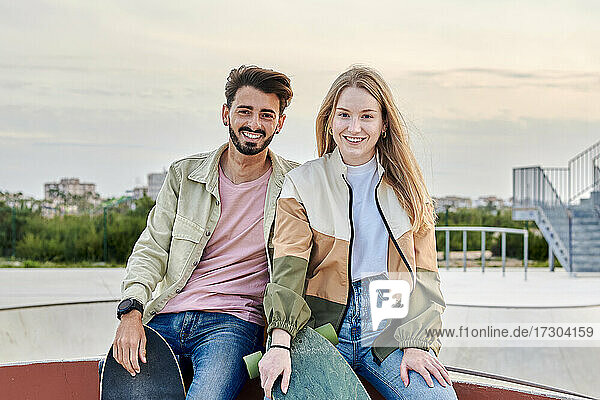 Junges gemischtrassiges Paar schaut lächelnd in die Kamera in einem Skatepark
