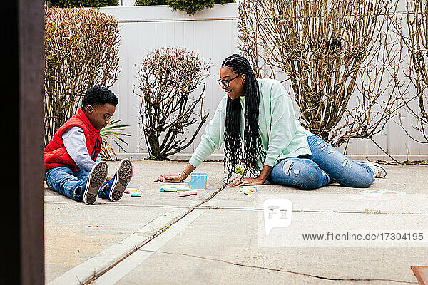 Mother and son playing with colorful chalks in backyard
