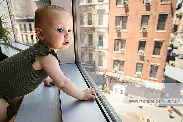 Neugierige glückliches Baby Mädchen schaut aus dem Fenster in der Stadt