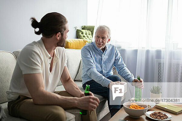 Ältere und junge Männer mit Bier im Gespräch auf der Couch