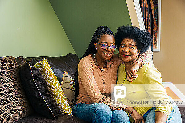 Porträt einer lächelnden älteren Frau mit Tochter  die zu Hause auf dem Sofa sitzt