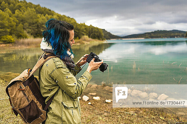 Tourist mit Tasche in der Natur beim Fotografieren am Seeufer