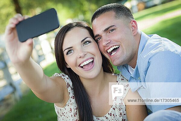 Glückliches gemischtrassiges Paar macht ein Selbstporträt mit einem Smartphone im Park