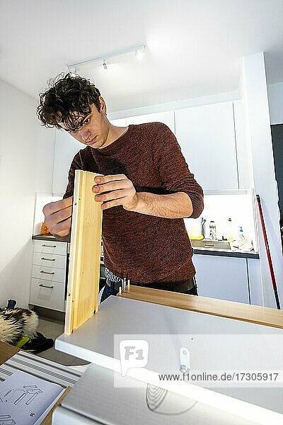 Junger Mann beim Heimwerken in seiner Wohnung  beim Zusammenbauen eines Regals