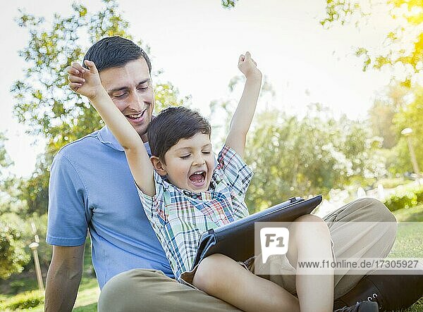 Handsome mixed-race father and son playing on a computer tablet outside