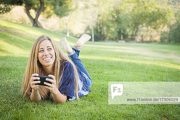 Lächelnde junge Frau mit Handy im Freien im Park