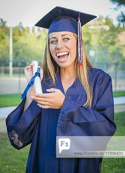 Excited and expressive young woman holding diploma in cap and gown outdoors