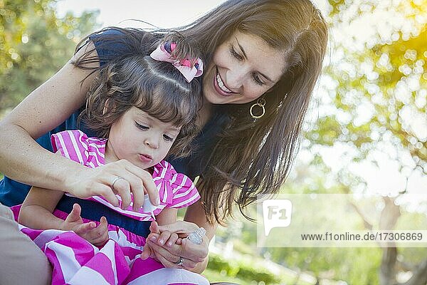 Gemischtrassige junge Mutter und niedliches Baby-Mädchen  das sich im Park die Fingernägel lackiert