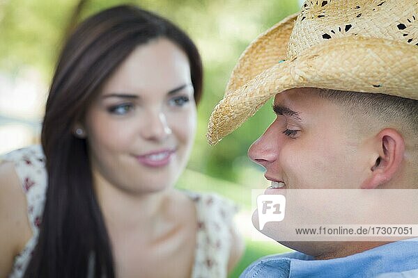 Glückliches gemischtrassiges romantisches Paar mit Cowboyhut flirtet im Park