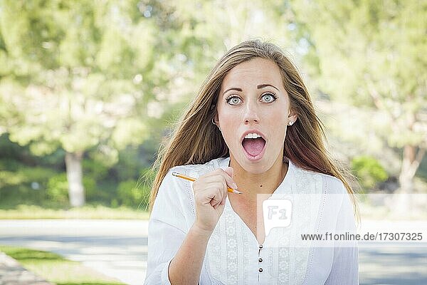 Aufgeregte junge Frau mit Bleistift im Freien im Park