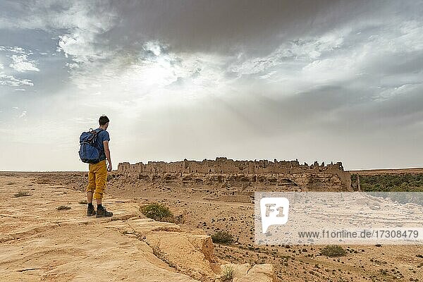 Junger Mann an einer Felsabbruchkante  hinten Ruinen der alten Stadt an der Oase Source Bleu  Blaue Quelle  Madkhal Meski  Marokko  Afrika
