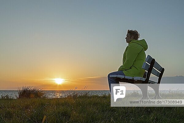 Frau genießt den Sonnenuntergang auf einer Bank  Großenbrode Weststrand  Schleswig-Holstein  Deutschland  Europa